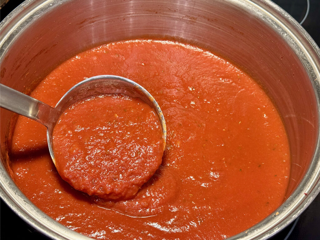 Ladle of quick red wine tomato sauce in stainless steel pot.