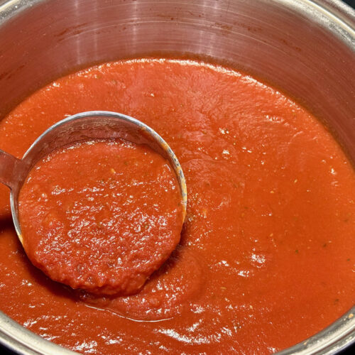 Ladle of quick red wine tomato sauce in stainless steel pot.