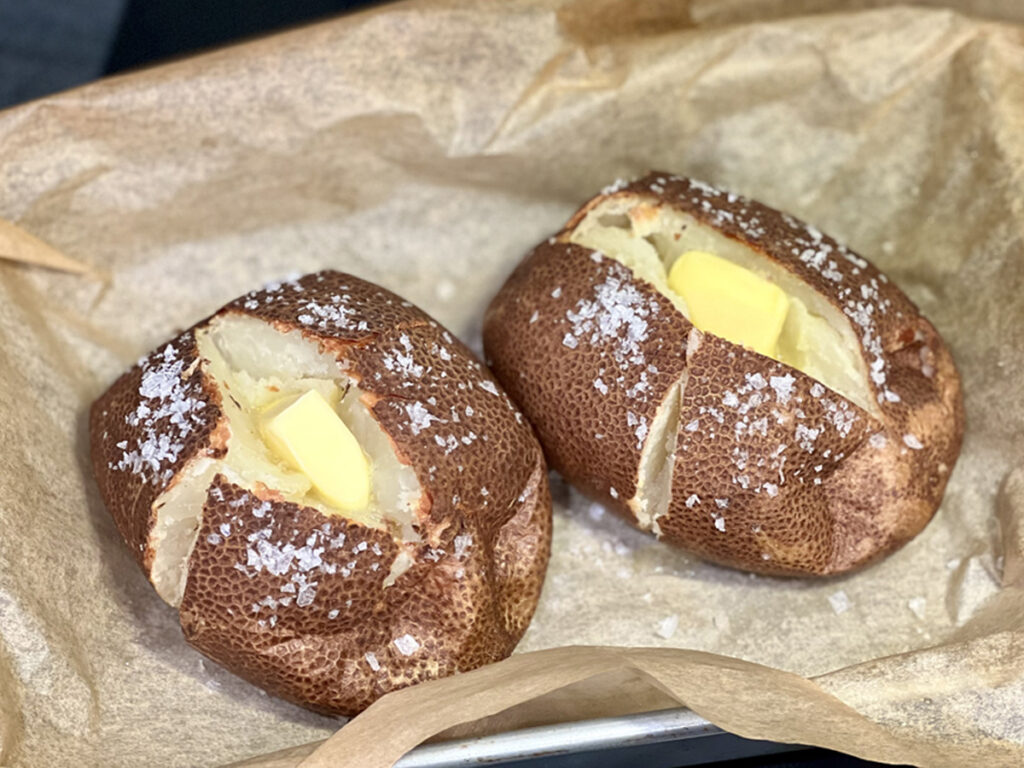 Steakhouse baked potatoes with salt jacket cut open with butter on parchment paper.