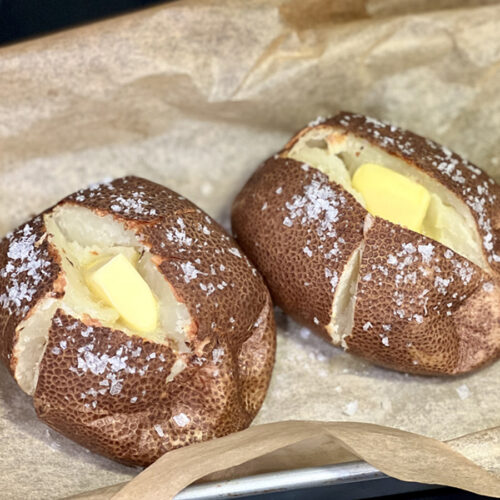 Steakhouse baked potatoes with salt jacket cut open with butter on parchment paper.