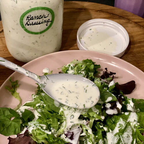 Large tablespoon of Homemade Dairy-Free Ranch Dressing (Whole30 compliant) drizzeled over mixed greens on a neutral plate.