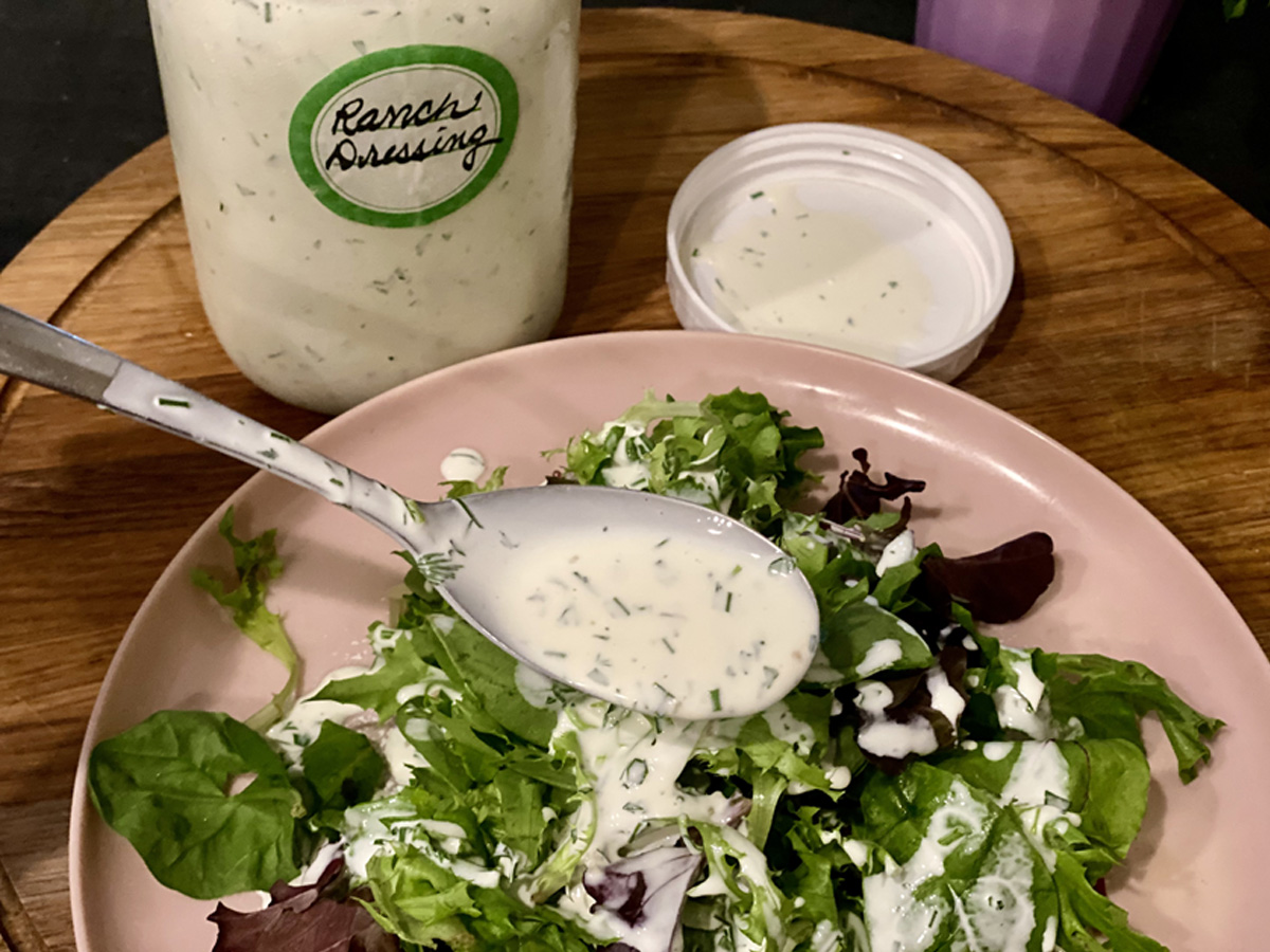 Tablespoon full of Dairy-Free Ranch Dressing (Whote30 - Paleo) friendly, drizzled over a mixed green salad on a neutral plate on a wood cutting board.