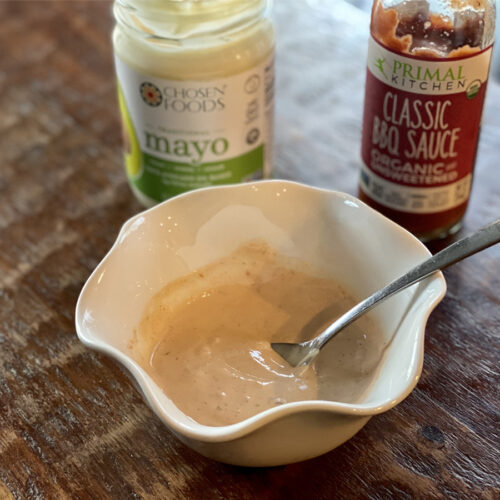 White scalloped bowl filled with The Best Two-Ingredient Fry sauce on a wood table with mayonnaise and bbq sauce bottles in the background.