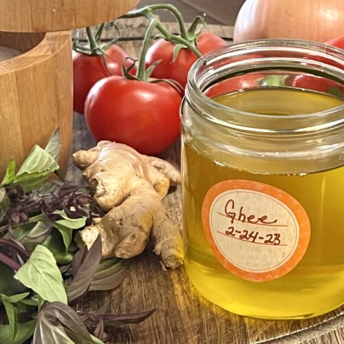 Ghee in a small glass jar surrounded by fresh Thai basil, ginger, and tomatoes.