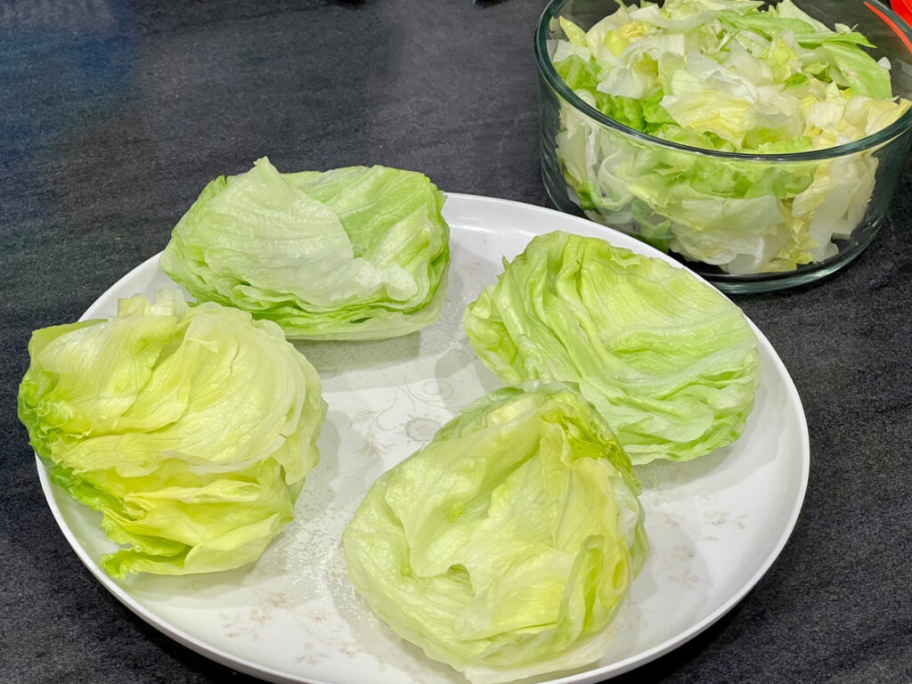 Two lettuce buns on a white plate with a small bowl of chopped lettuce on the side