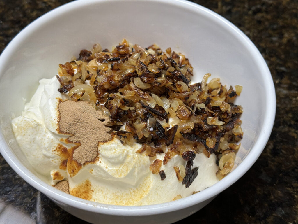 Sour cream, onions, beef bouillon base in a white bowl