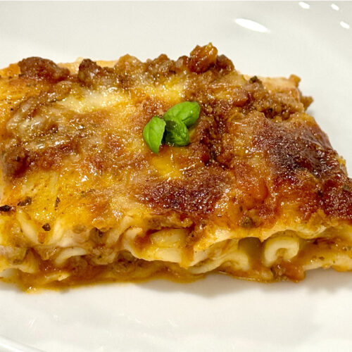 Slice of kid friendly three layer lasagna on a white plate with a tiny garnish of basil