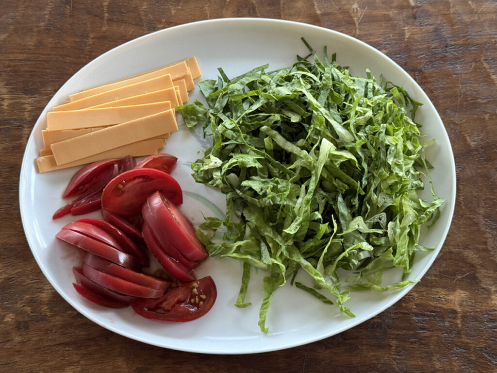 A platter of sliced cheese, shredded lettuce, and sliced tomatoes for tacos.