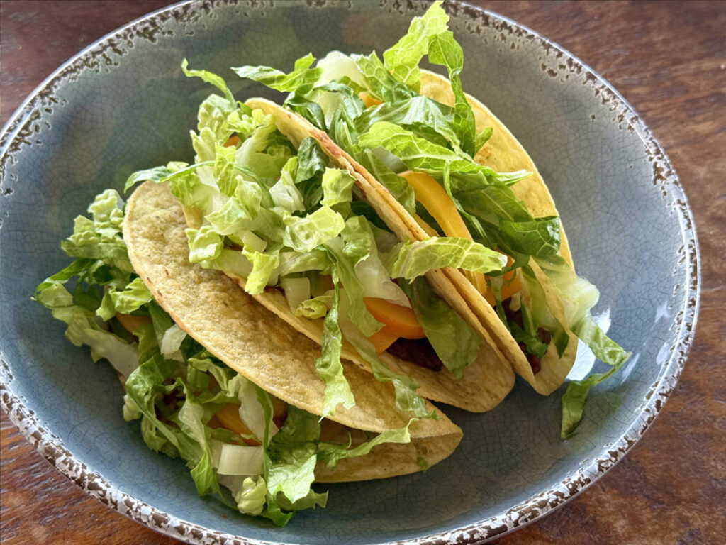 Plate of three crunch ground beef tacos with lettuce and cheese.